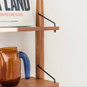 Wooden shelf by Born in Colour featuring metal support brackets with a brown and blue glass pitcher and a book